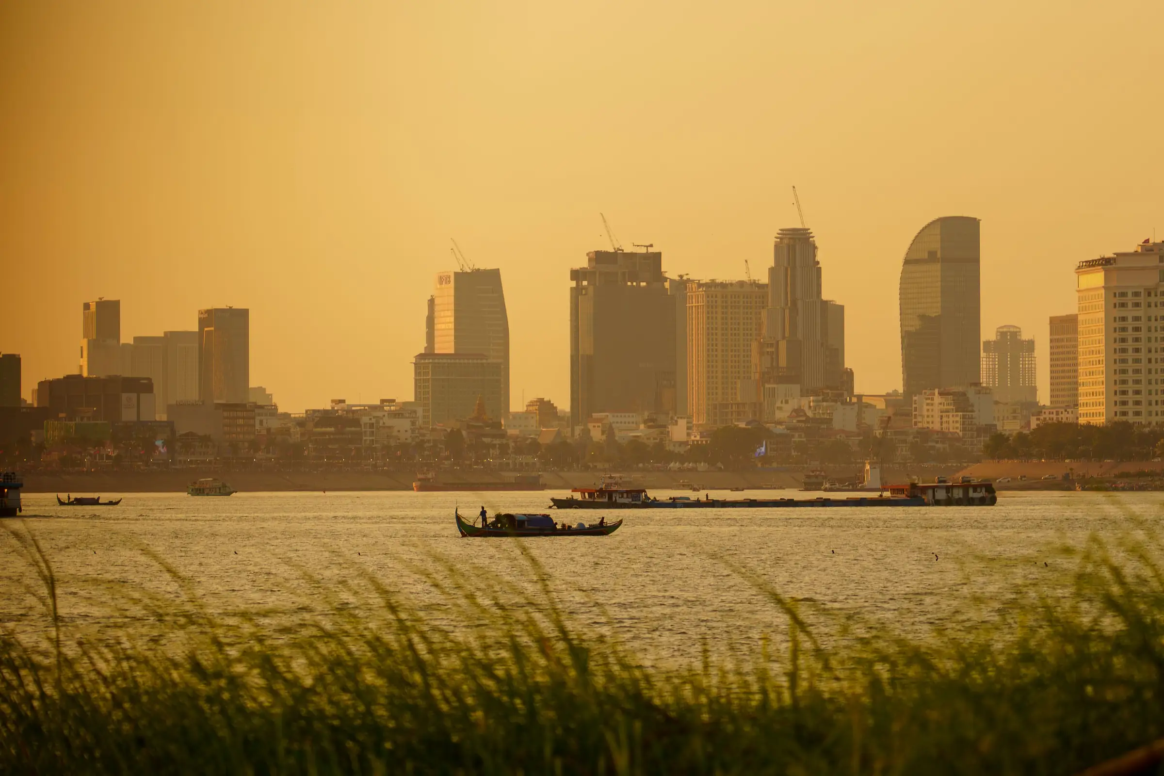 The Phnom Penh skyline at sunset, seen across the river, with boats on the water