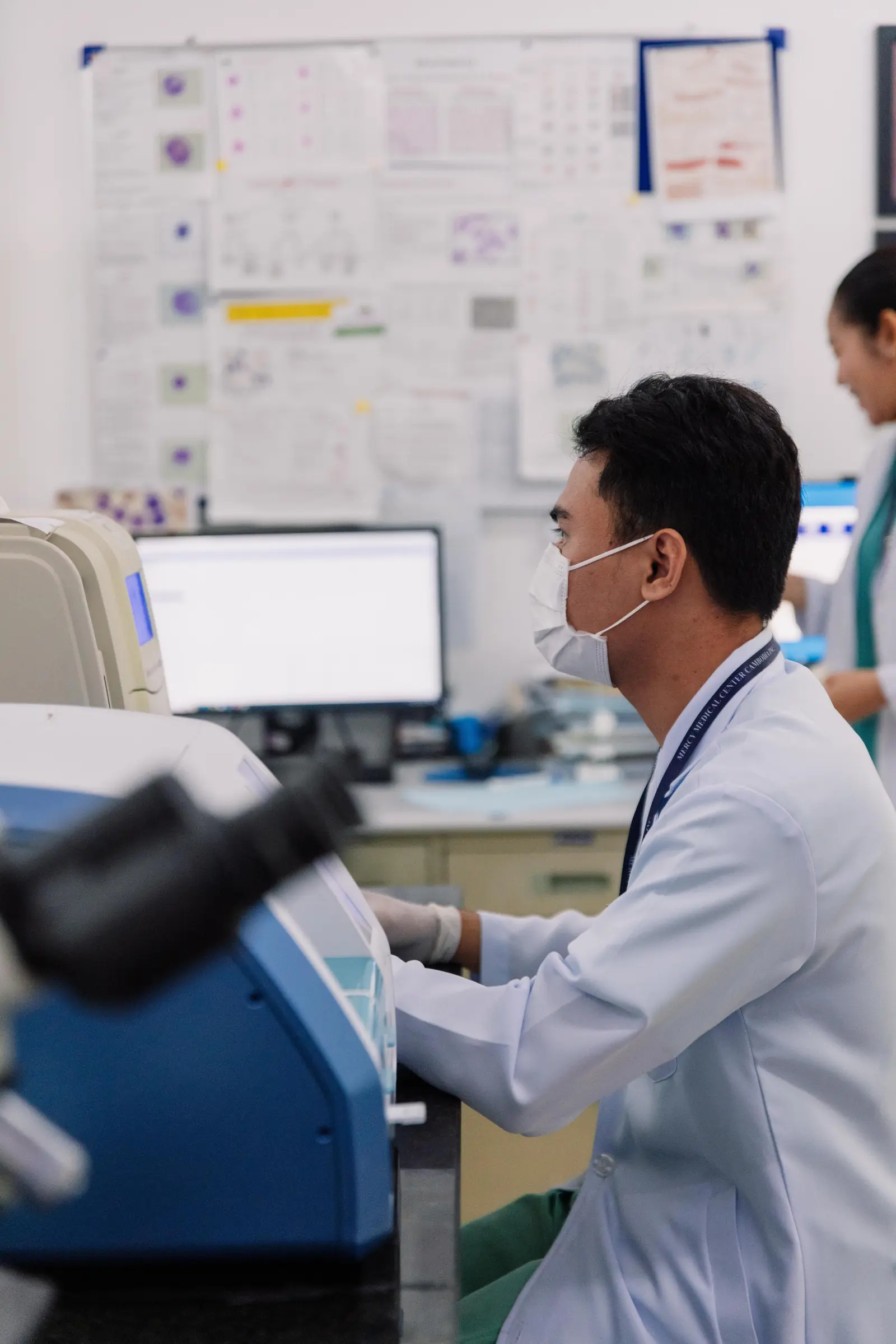 A laboratory technician in a white coat and mask working at a machine in a medical laboratory in Phnom Penh, Cambodia